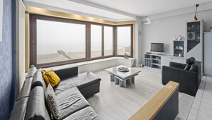 Ein modernes Wohnzimmer mit großem Fenster, einer Couch, einem Couchtisch und einem Fernseher.