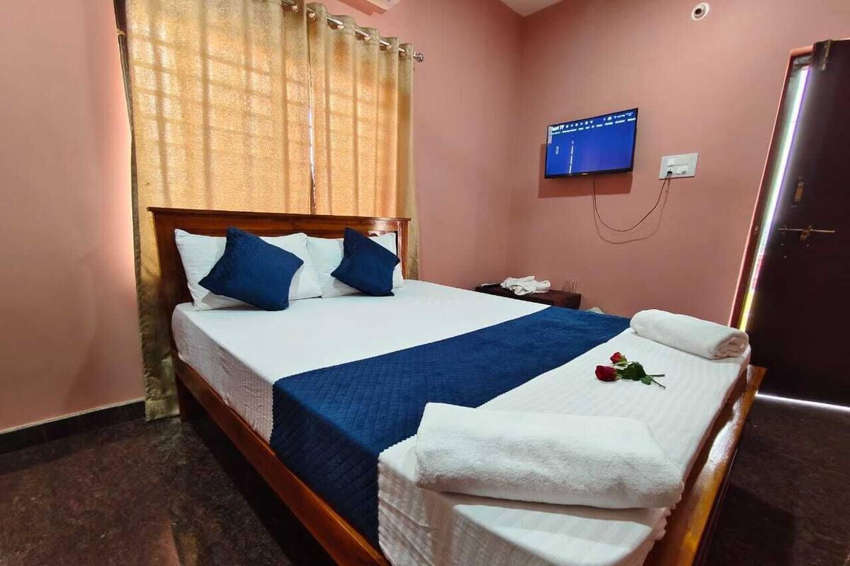 A double bed with blue bedding, a TV on the wall, and a small desk with a phone.