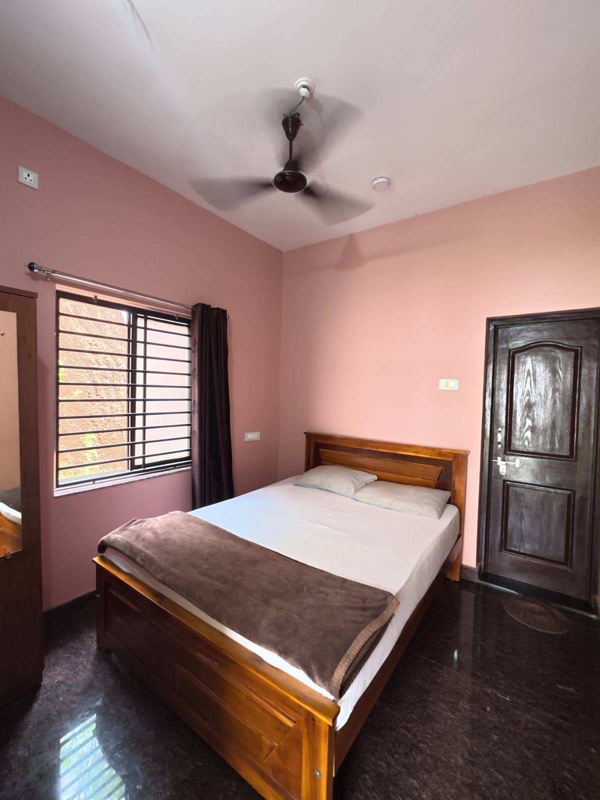 A bedroom with a bed, a ceiling fan, a window with bars, and a door.