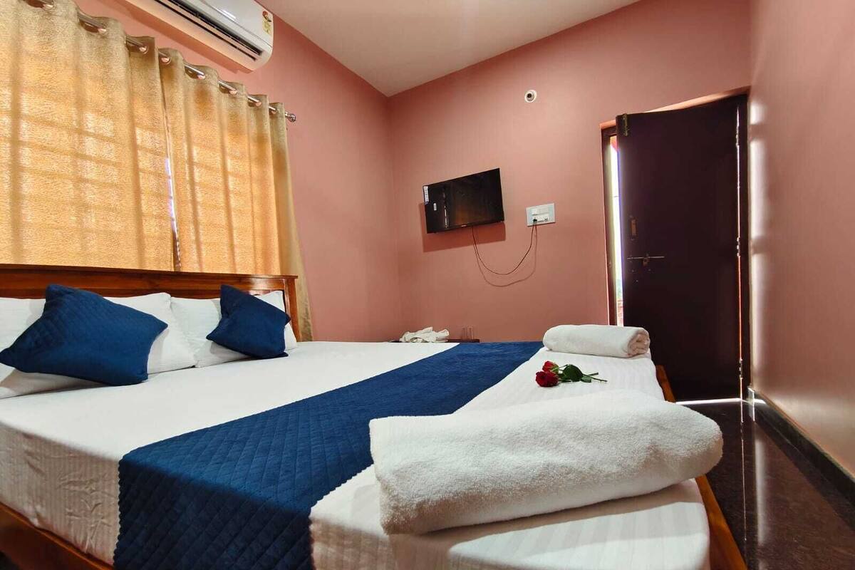 A hotel room with a bed, a TV, a door, and an air conditioning unit.