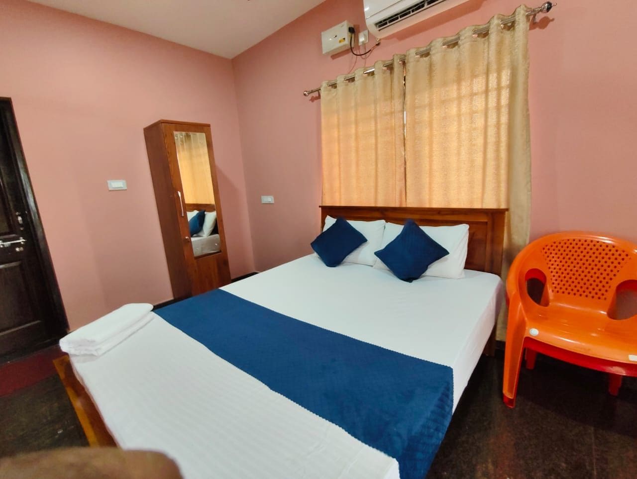 Quarto de hotel com cama, cadeira, espelho e ar condicionado.