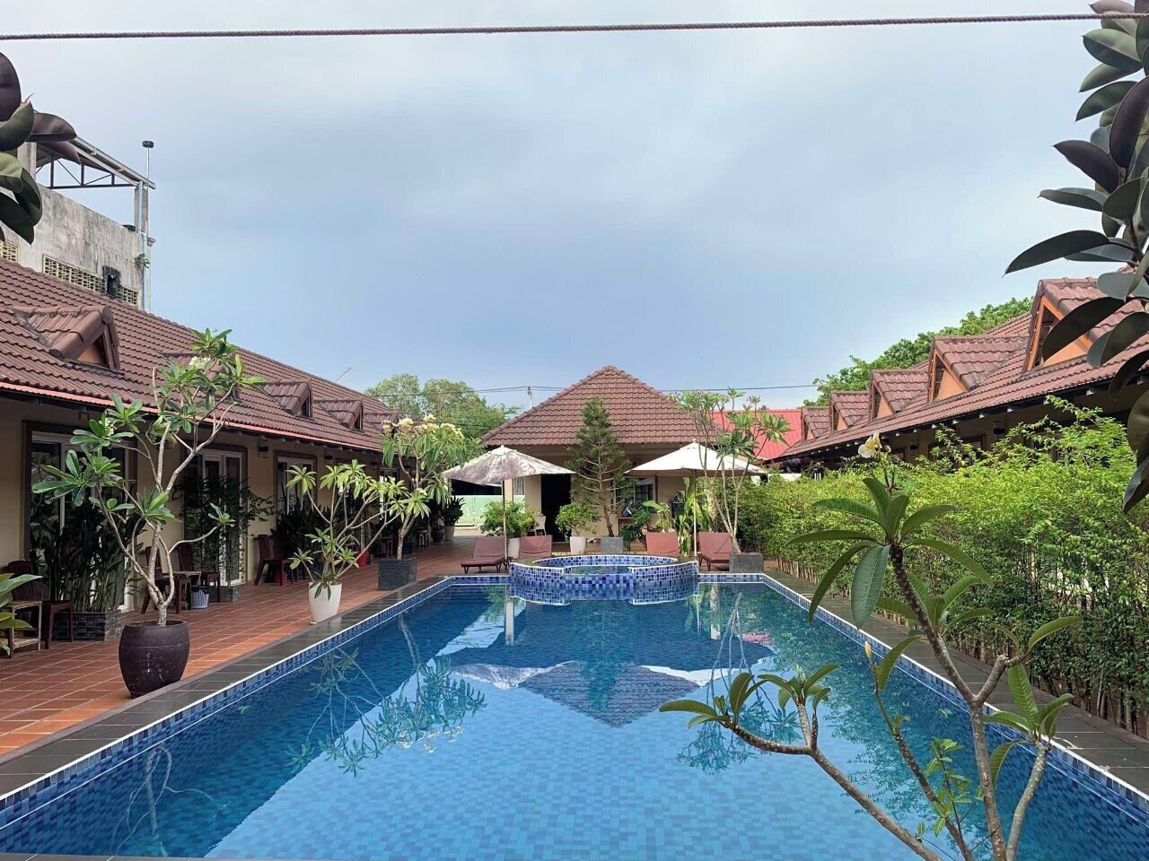 A swimming pool with tiled edges, surrounded by potted plants and outdoor seating areas.