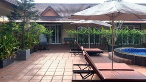 Un espacio al aire libre techado con piso de baldosas, sillas de lounge de madera y sombrillas.