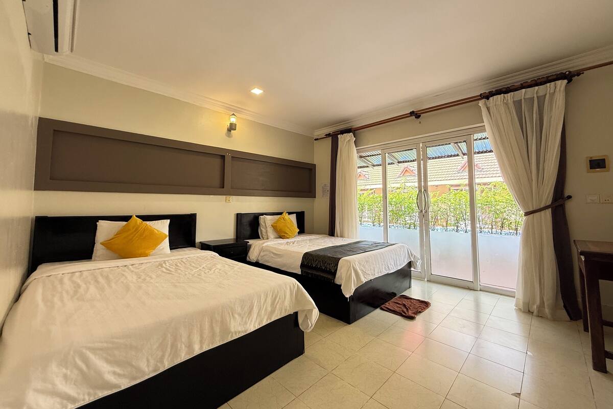 A hotel room with two beds, a large window with curtains, and a view of the outside.