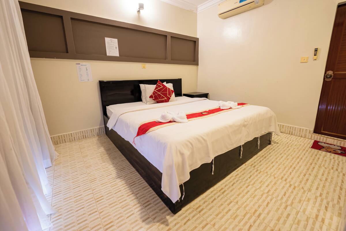 A hotel room with a bed, a nightstand, a wall-mounted air conditioner, and a door.