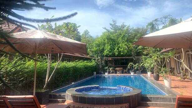 Una piscina rectangular con un jacuzzi, rodeada de exuberante vegetación y protegida por grandes sombrillas.