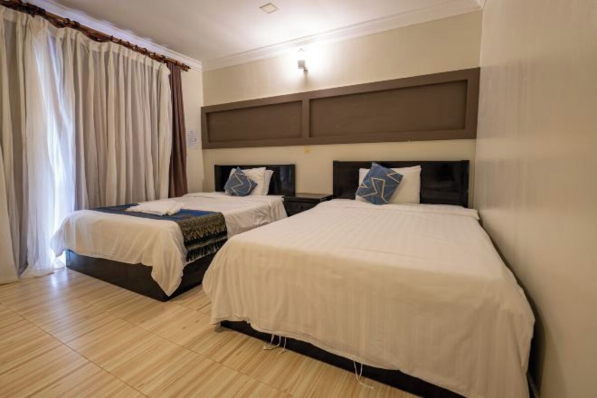 A hotel room with two beds, a wooden floor, and a large window with curtains.
