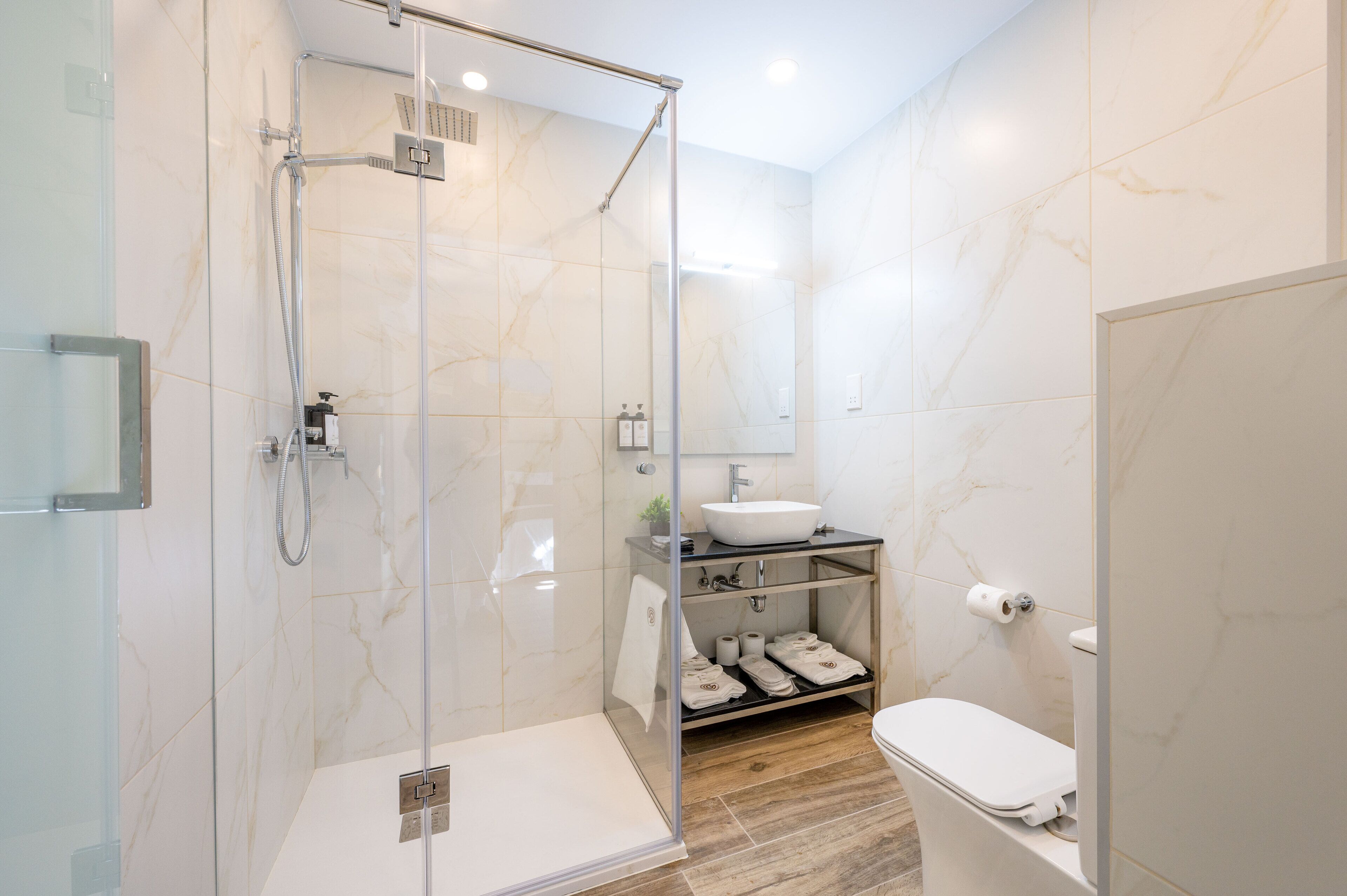 A modern bathroom with a glass-enclosed shower, a white sink, and a toilet.