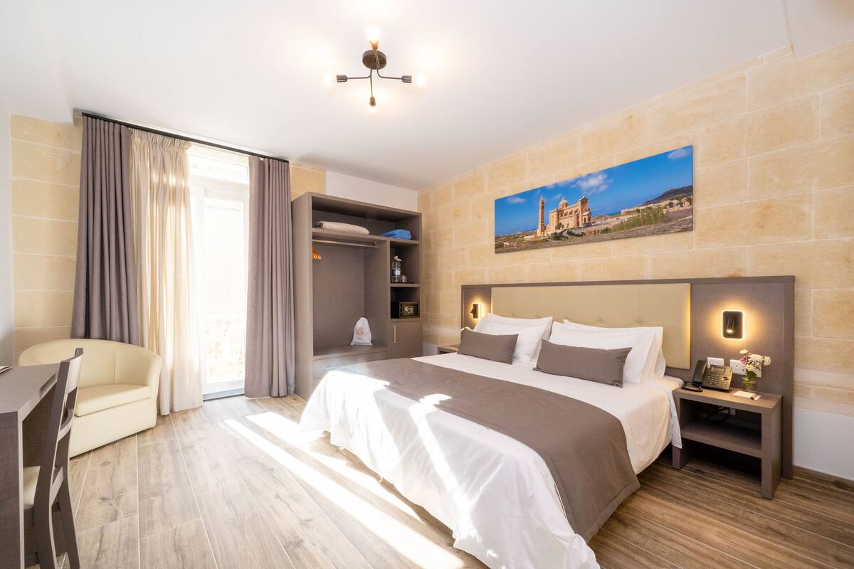 Una habitación de hotel con una cama, una mesita de noche y un cuadro de un edificio en la pared.