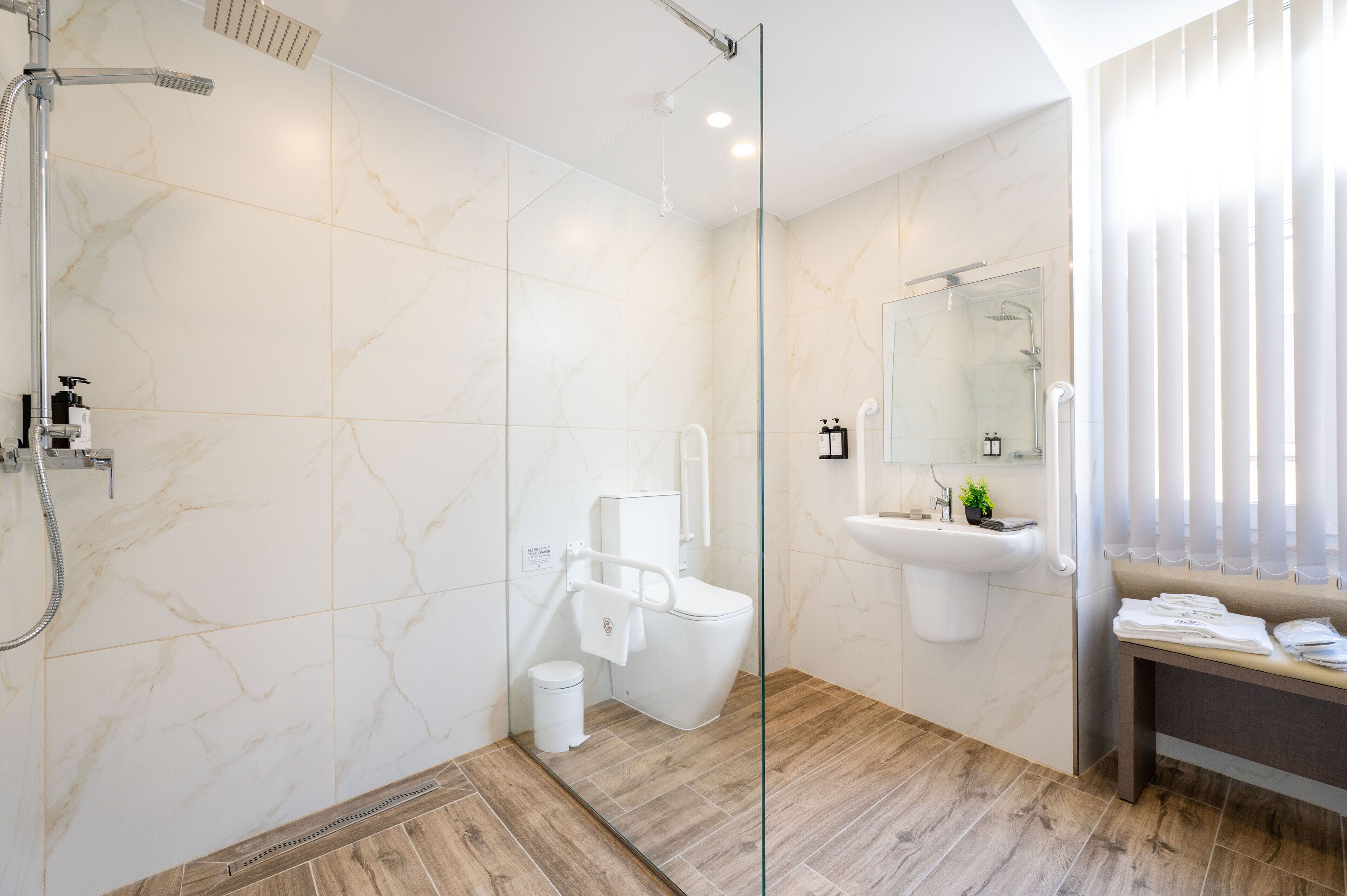 Un baño moderno con cabina de ducha de vidrio, inodoro, lavamanos y un banco con toallas.