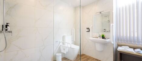 Un baño moderno con cabina de ducha de vidrio, inodoro, lavamanos y un banco con toallas.