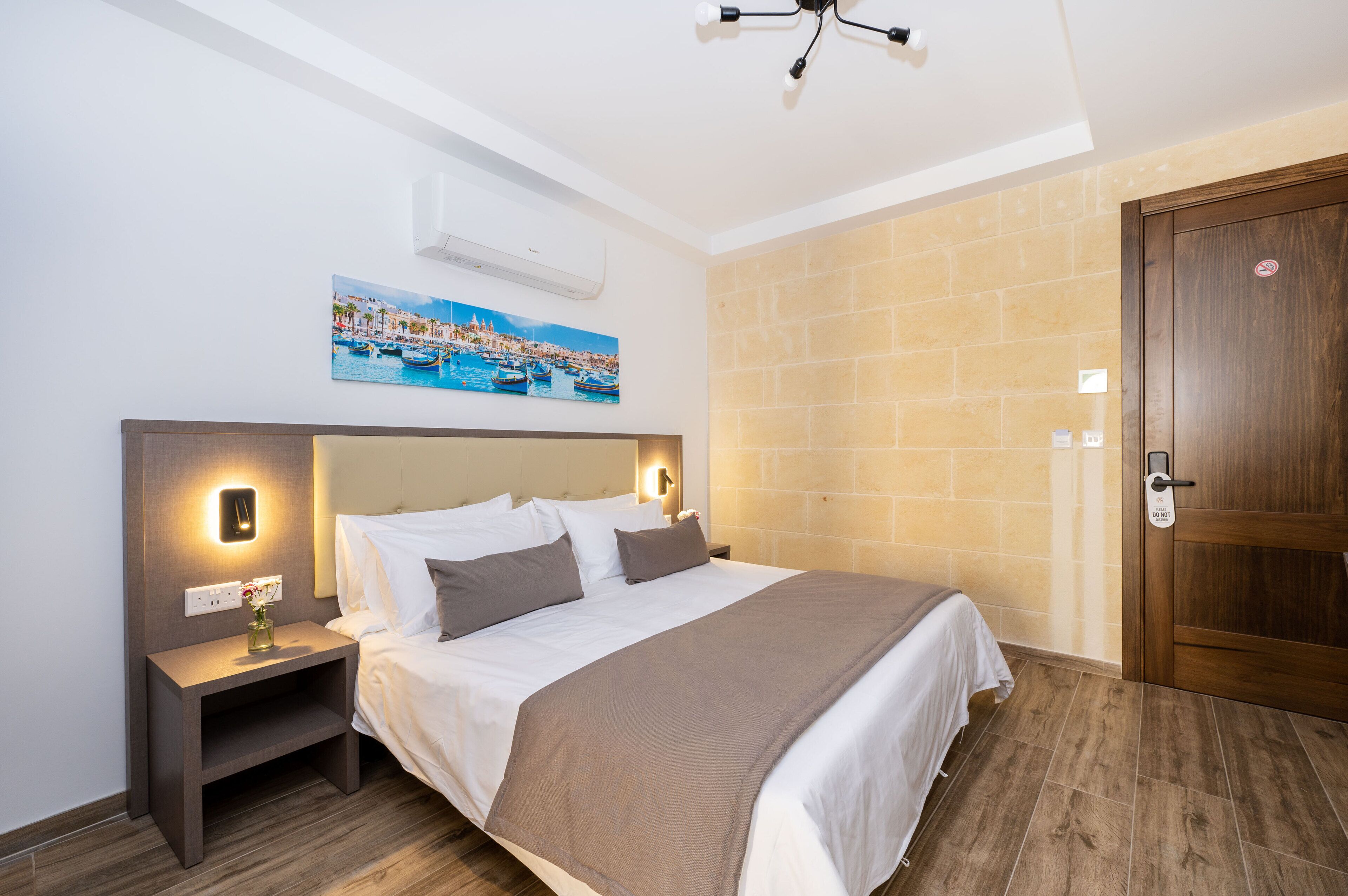 Quarto de hotel com cama, mesa de cabeceira, ar condicionado fixado na parede e uma porta.
