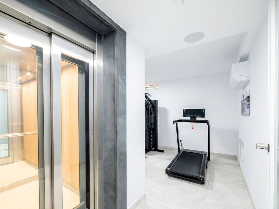 Een lift met glazen deuren, een loopband en een wandairconditioner in een modern interieur.