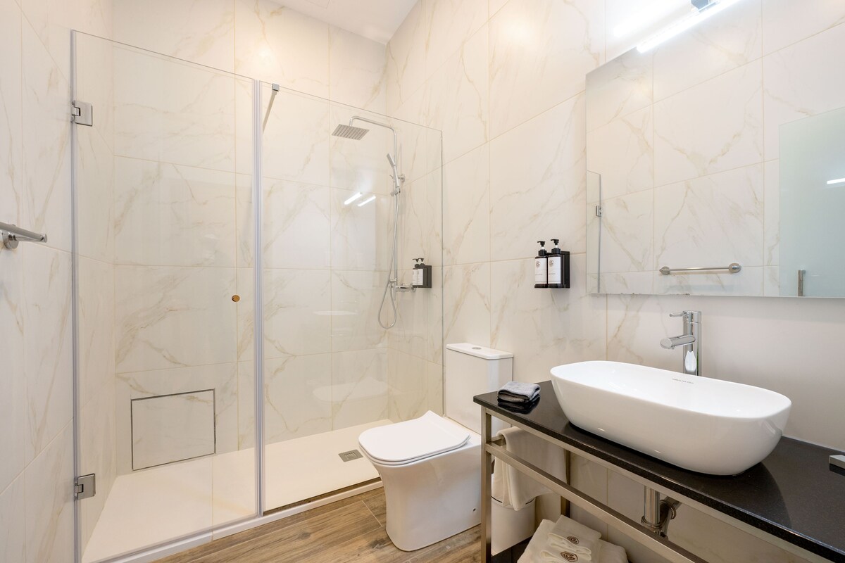 Un baño moderno con ducha de vidrio, un lavabo blanco y pared revestida de mármol.