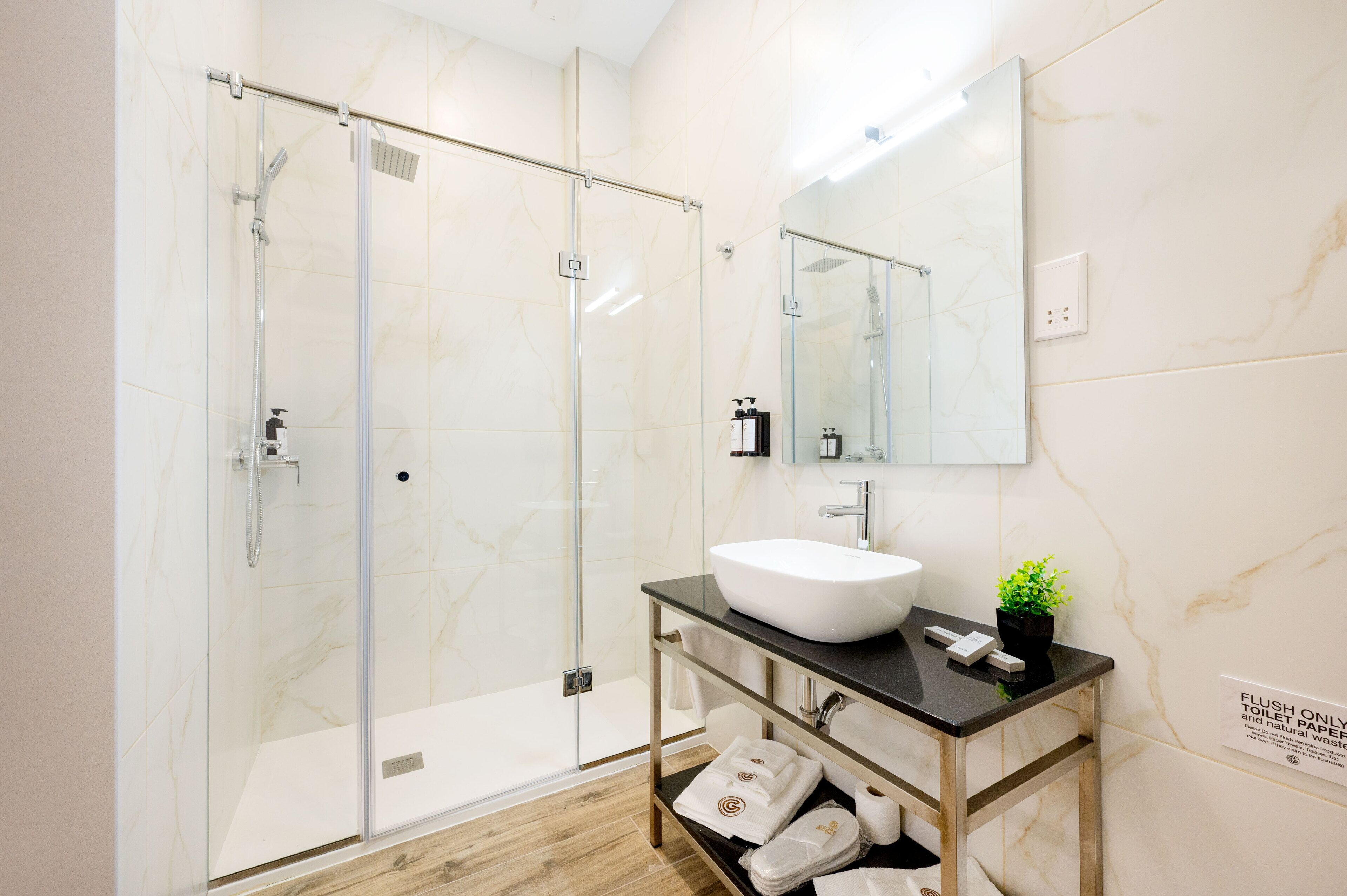 Een moderne badkamer met een douchecabine van glas, een witte wastafel en een spiegel erboven.