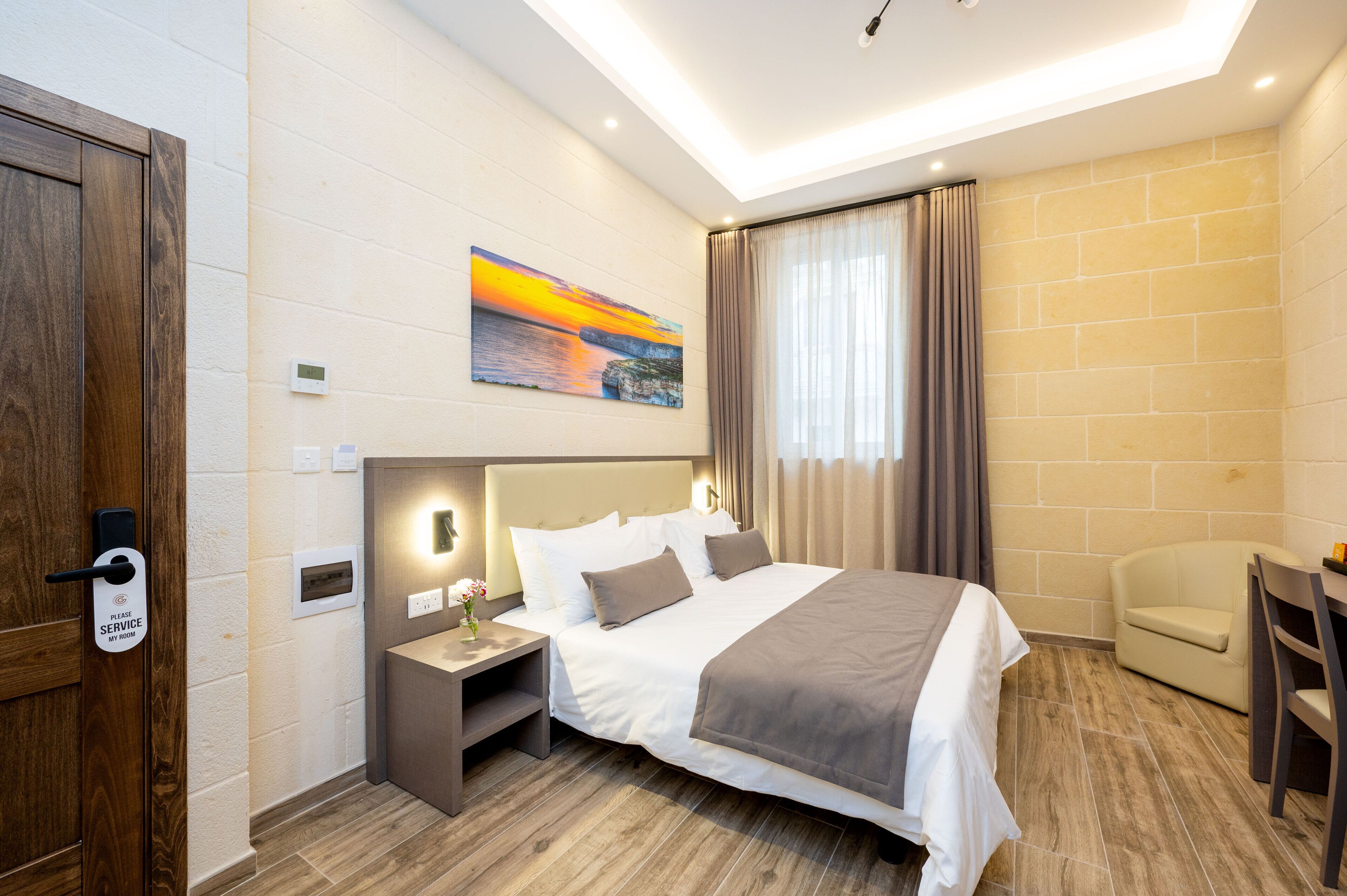 A hotel room with a bed, bedside table, nightstand, and a chair.