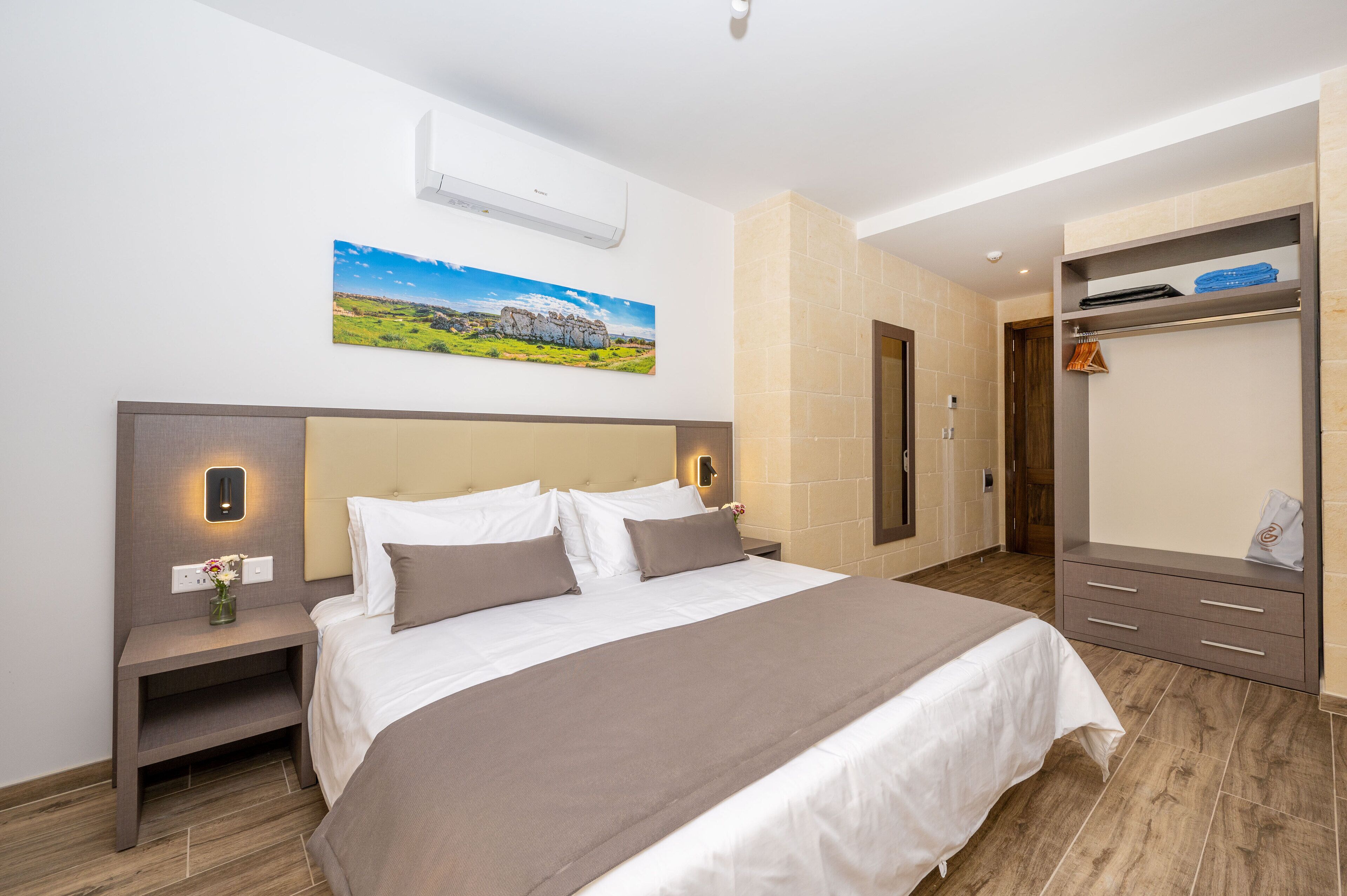 Ein modernes Hotelzimmer mit einem großen Bett, einem Nachttisch mit Blumenvase, einem Kleiderschrank und einem Bild an der Wand.