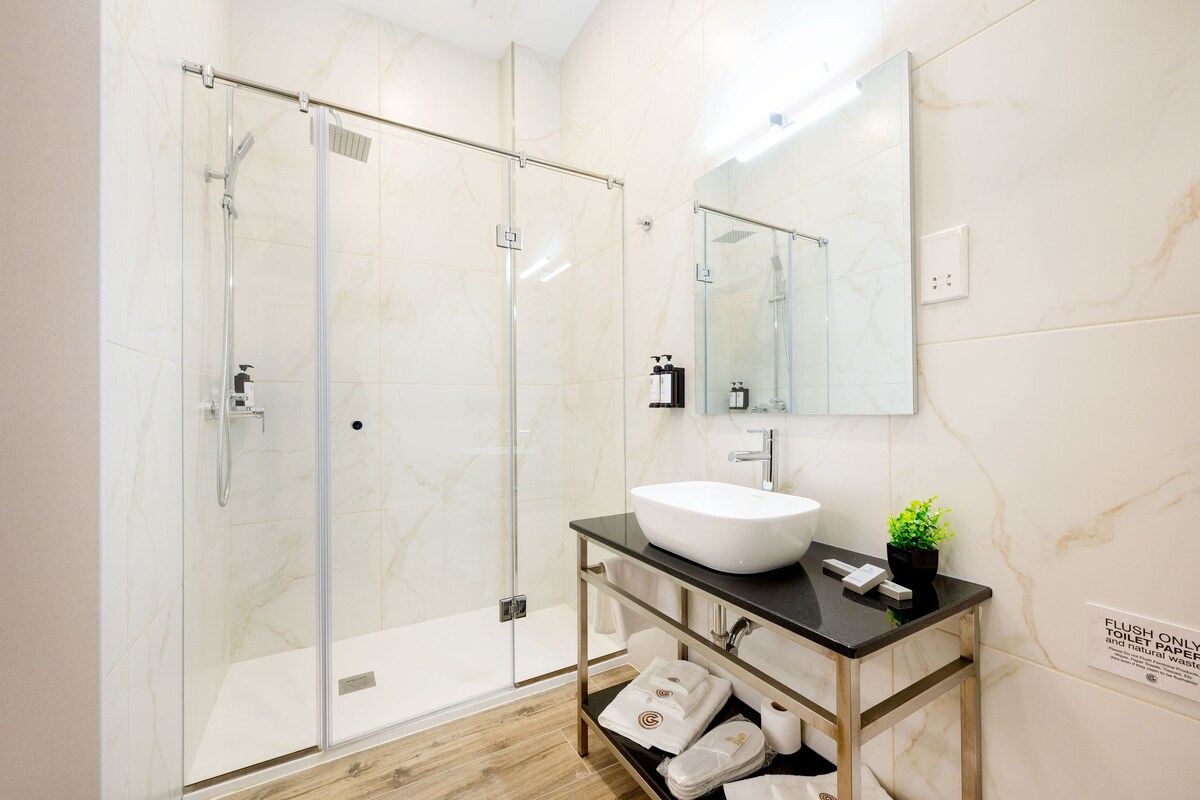 A modern bathroom with a glass-enclosed shower, a white sink, and a mirror above it.