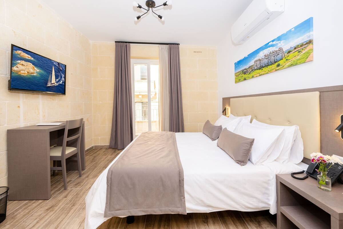 Habitación de hotel con cama, escritorio, silla, televisor y un cuadro en la pared.