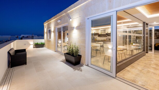 A modern building with a glass facade, outdoor seating area, and a well-lit interior. - C4 Retreats Gozo (Xaghra)