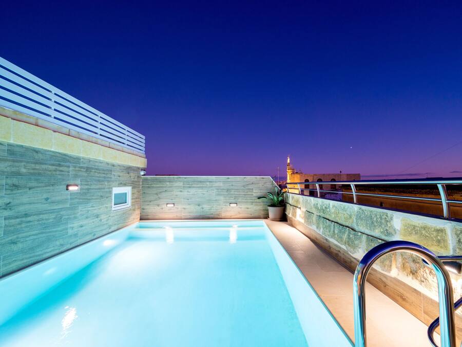 Una piscina interior con pared de madera y pared de piedra, barandilla de metal y vista del horizonte urbano al anochecer.