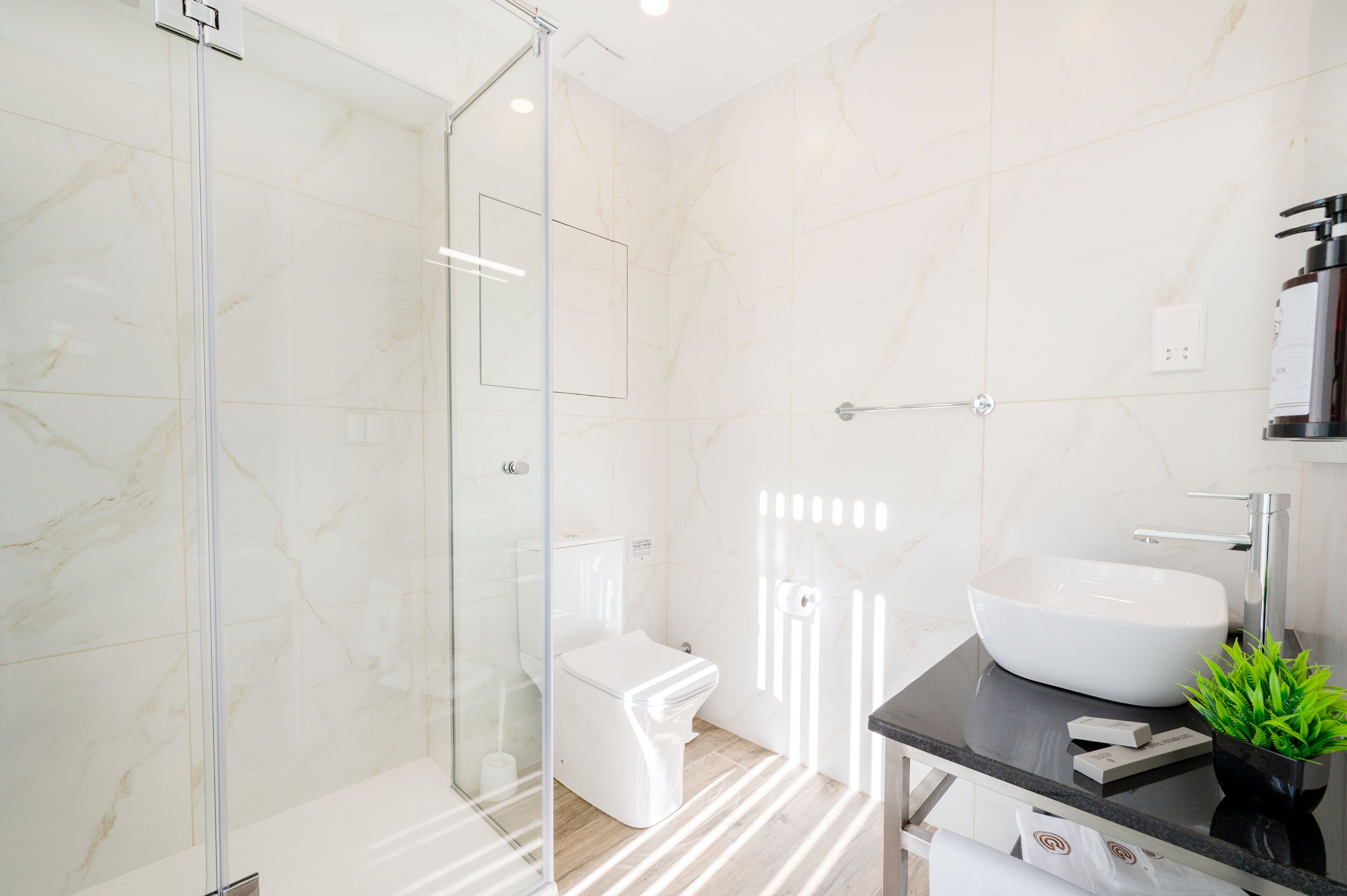 Un baño moderno con cabina de ducha de vidrio, inodoro blanco y un lavamanos grande sobre una encimera negra.