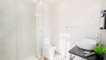Un baño moderno con cabina de ducha de vidrio, inodoro blanco y un lavamanos grande sobre una encimera negra.