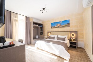 A hotel room with a large bed, a desk with a coffee maker, a wardrobe, and a painting of a building on the wall. - C4 Retreats Gozo (Xaghra)