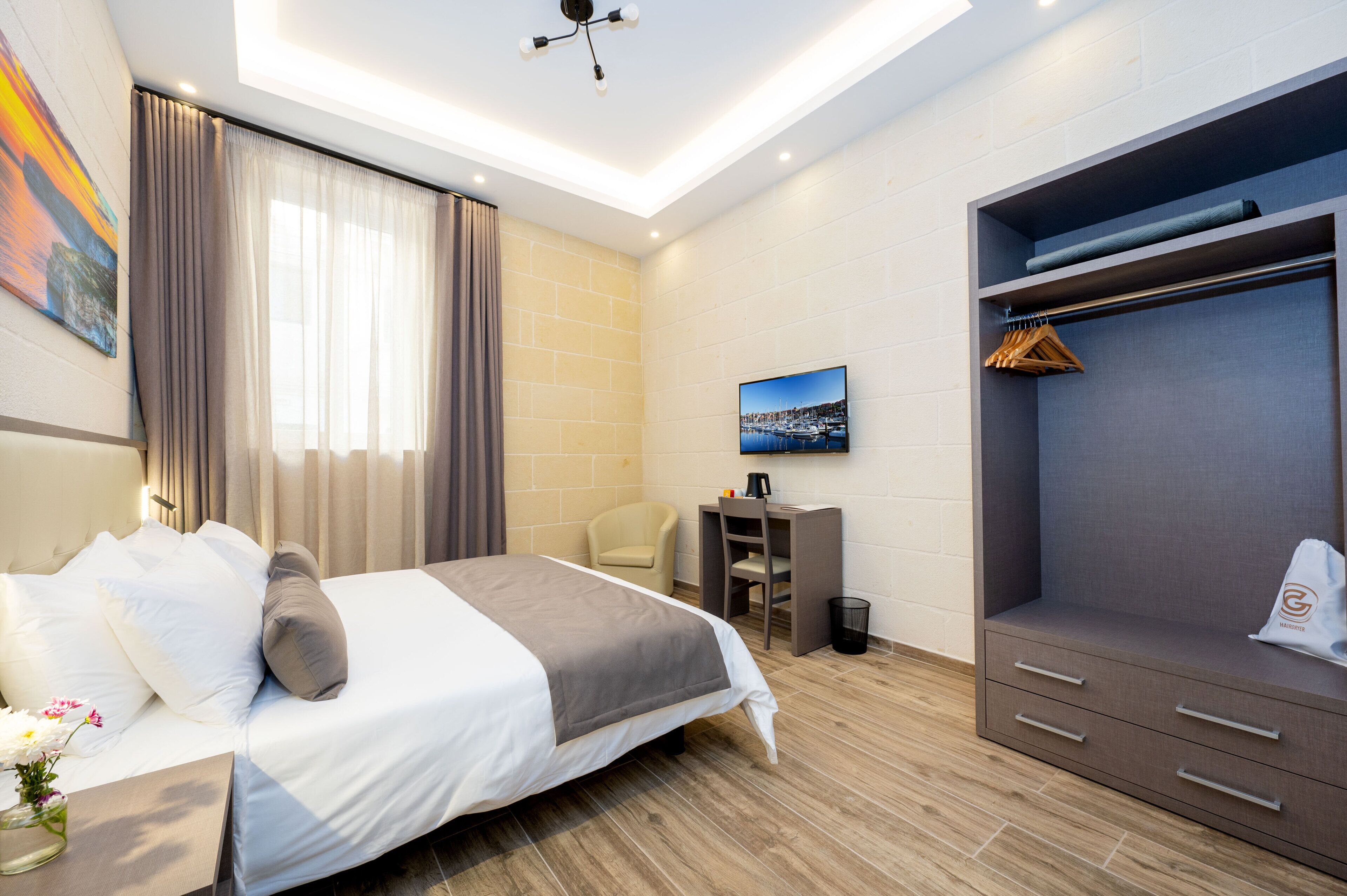 A modern hotel room with a bed, a desk, a wardrobe, and a TV on the wall.
