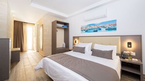 A hotel room with a large bed, a desk with a phone, and a painting of a coastal town. - C4 Retreats Gozo (Xaghra)