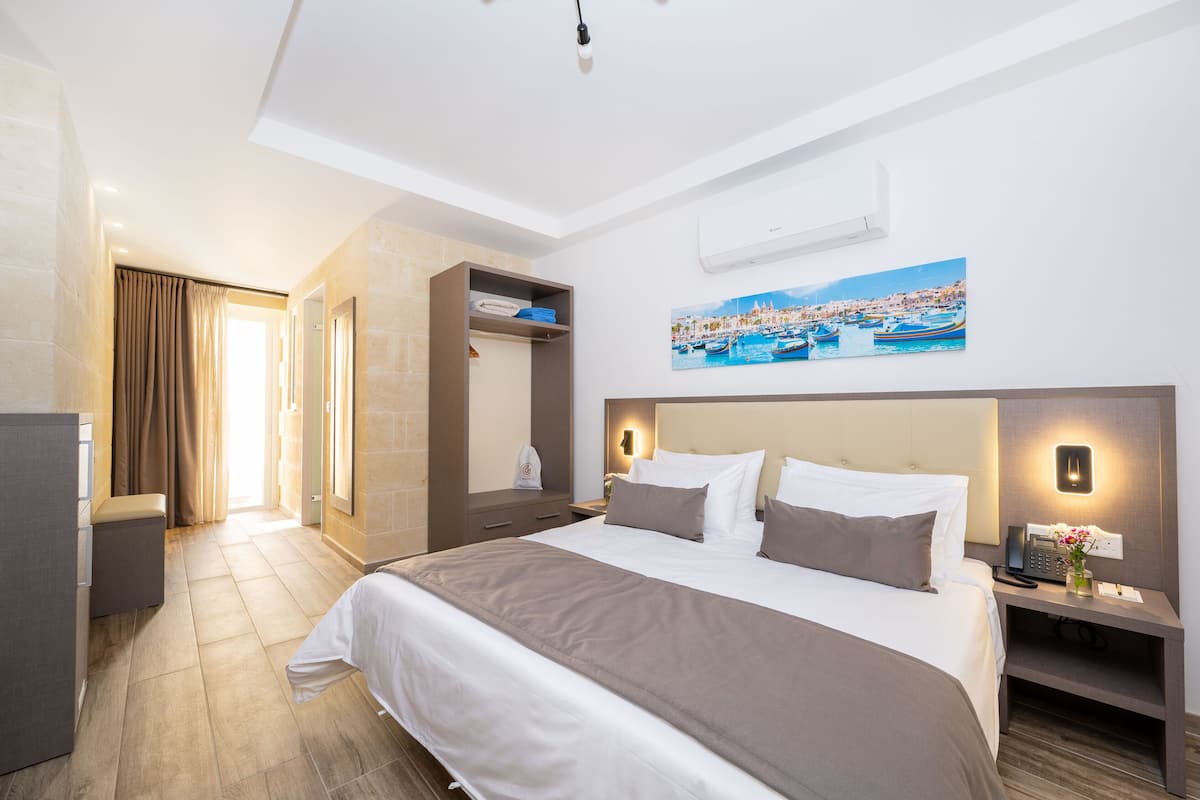 Habitación de hotel con una cama grande, un escritorio con teléfono y un cuadro de una ciudad costera.