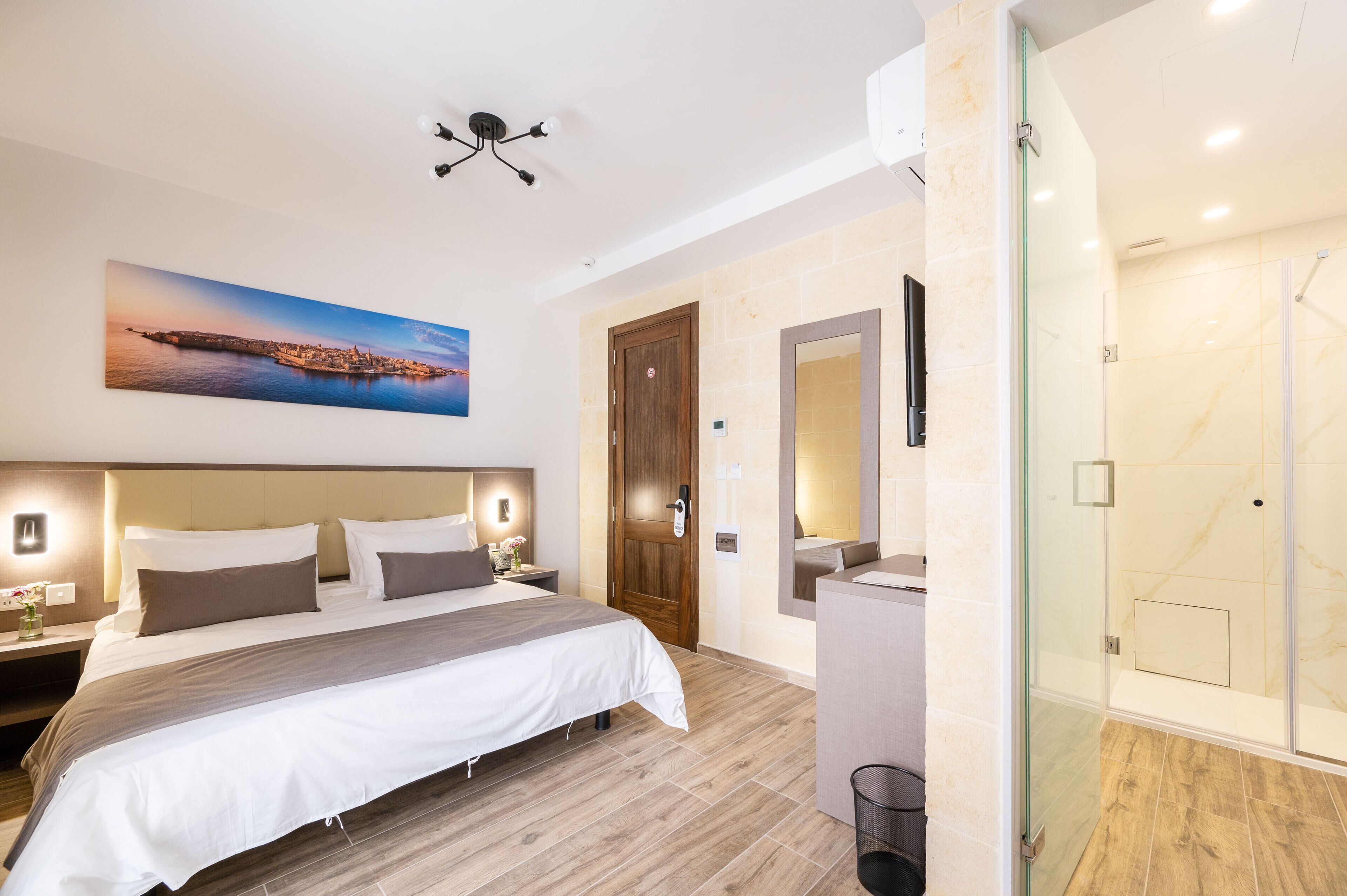A modern hotel room with a large bed, a glass shower enclosure, and a cityscape painting on the wall.
