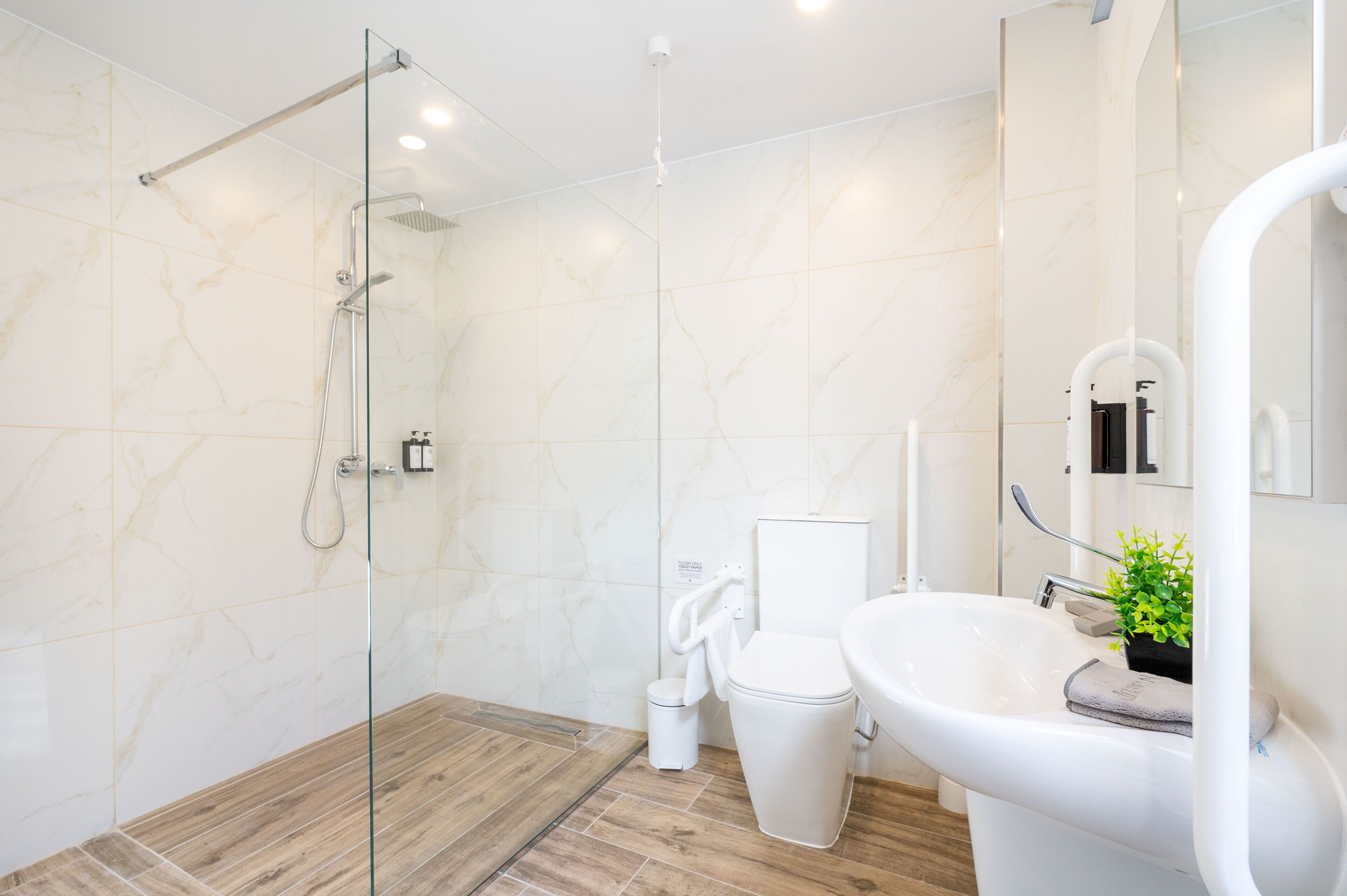 A modern bathroom with a glass-enclosed shower, a white toilet, and a sink with a mirror.