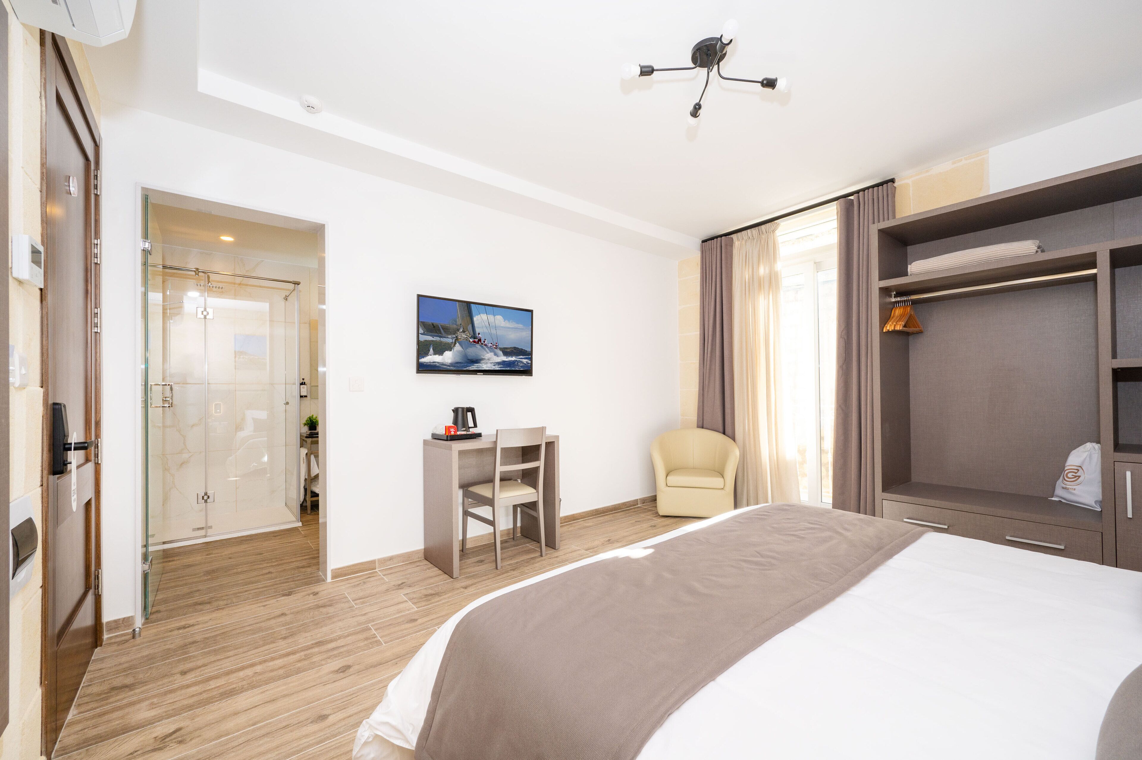 Una habitación de hotel con cama, escritorio con silla, perchero y armario.