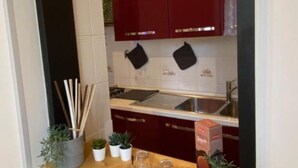 A kitchen with red cabinets, a stainless steel sink, and a countertop with a box of tissues. - AURELIA Residence (Roma)