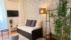 A modern bedroom with a sofa bed, a small table, a floor lamp, and a large plant. - AURELIA Residence (Roma)