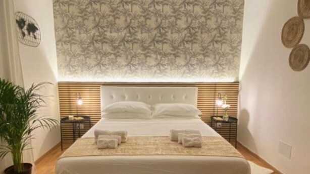 A hotel room with a large bed, bedside tables, a potted plant, and a patterned wallpaper. - AURELIA Residence (Roma)
