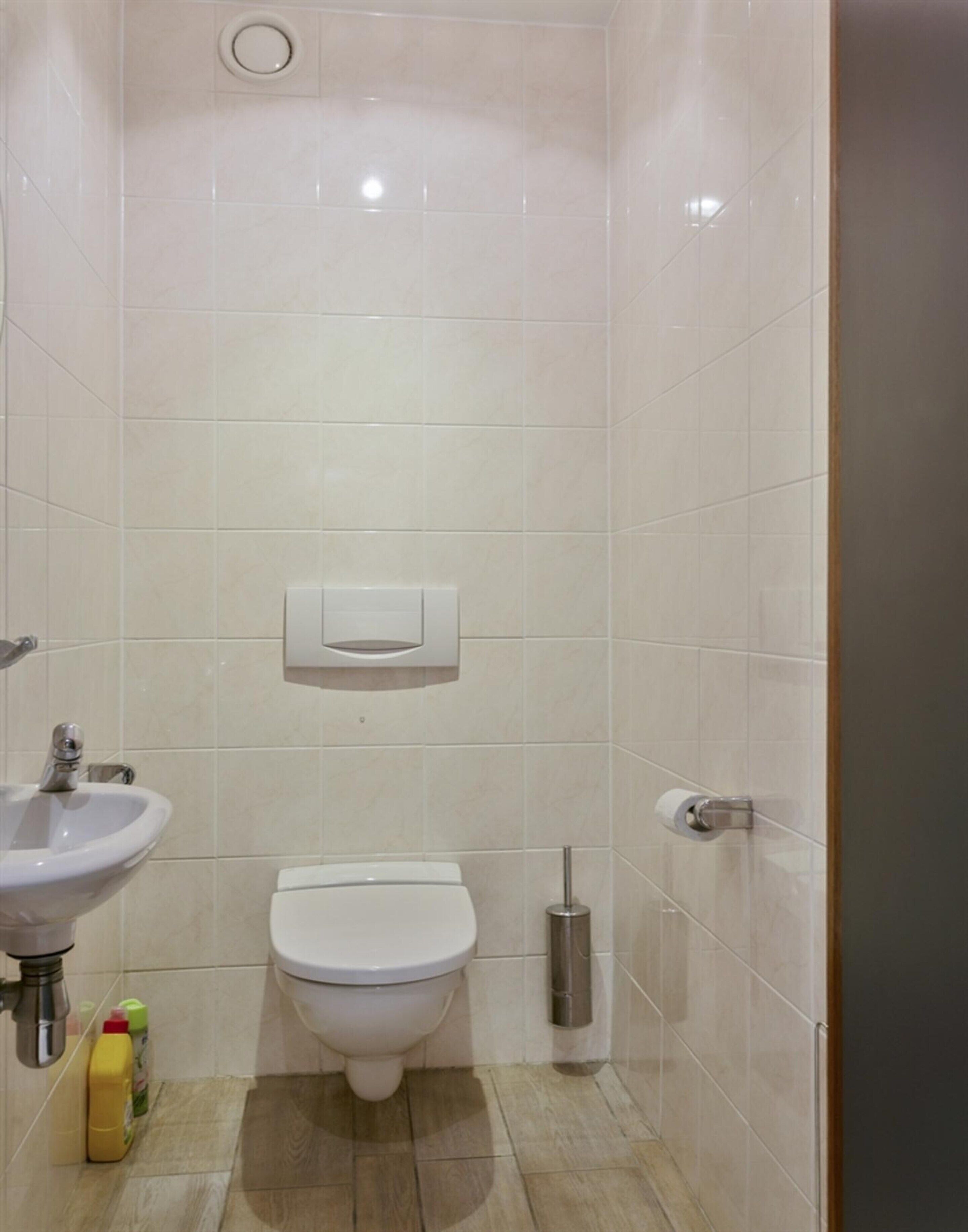 Une petite salle de bain moderne, équipée de toilettes, d’un lavabo et d’un porte-rouleau de papier toilette.