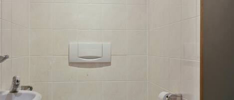 Une petite salle de bain moderne, équipée de toilettes, d’un lavabo et d’un porte-rouleau de papier toilette.