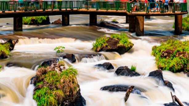 Un pont où des personnes observent une cascade.