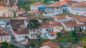Une ville où se dresse une église remarquable, dotée d’un clocher, entourée de bâtiments aux toits de tuiles rouges, le tout surplombé par un paysage vallonné.