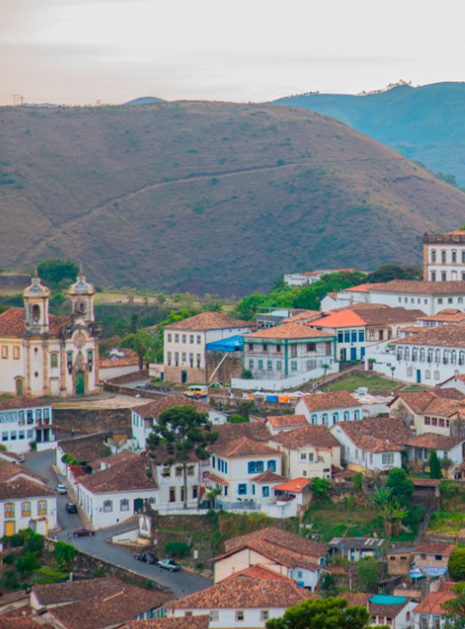 Un pueblo con una iglesia destacada que cuenta con un campanario, rodeado de edificios con tejados rojos y un paisaje montañoso al fondo.