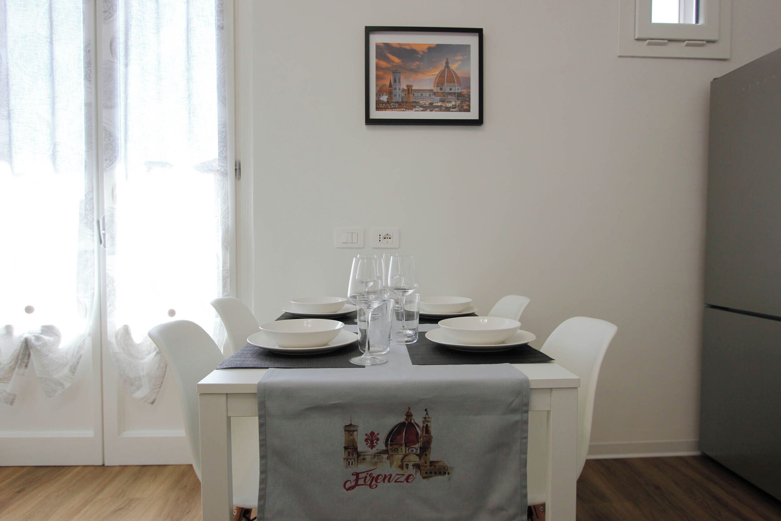 Une table à manger dressée avec des assiettes, des verres et une nappe ornée d’un motif représentant un paysage urbain.