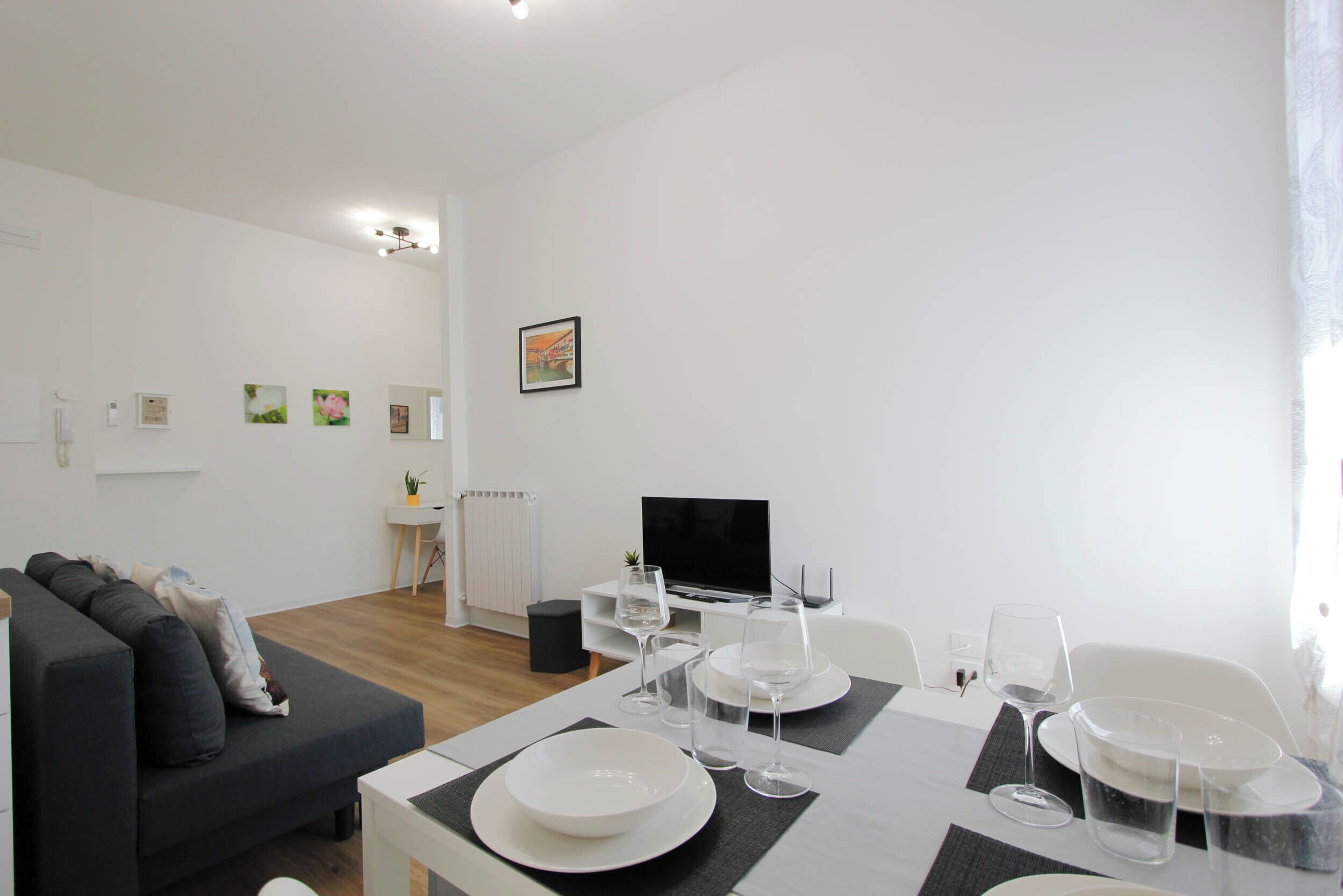 A modern living room with a dining table set for four, a sofa, a TV, and artwork on the wall.