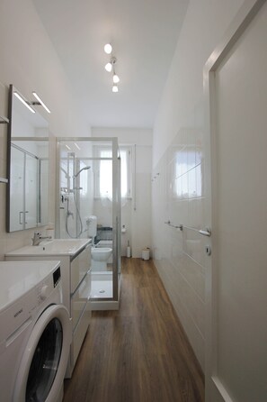 Uma casa de banho moderna com máquina de lavar roupa, sanita e zona de duche.