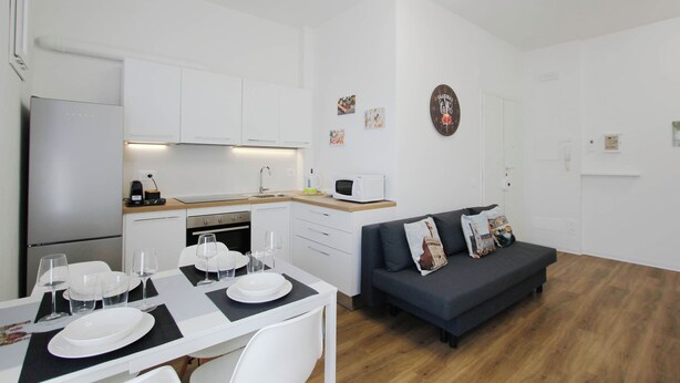 A modern kitchen with white cabinets, a microwave, and a dining area with a table set for four. - Casa Giotto (Scandicci)