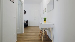 A hallway with a white wall, a small table with a potted plant, and a door at the end. - Casa Giotto (Scandicci)