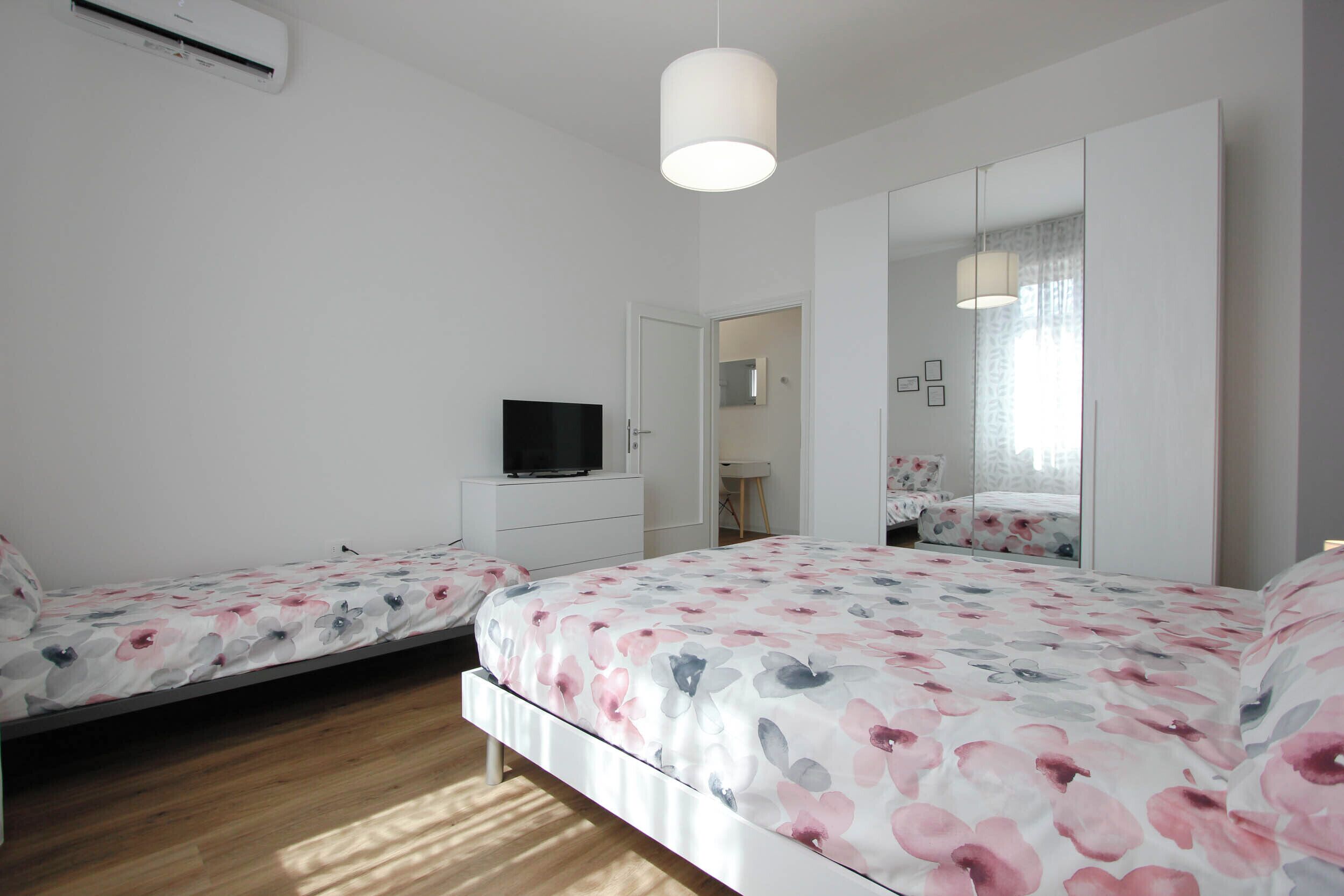 Een slaapkamer met twee bedden, een televisie, een kledingkast en een spiegel.