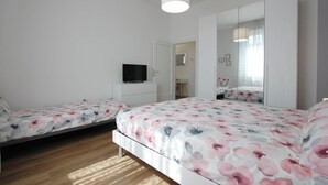 A bedroom with two beds, a TV, a wardrobe, and a mirror. - Casa Giotto (Scandicci)