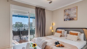 A hotel room with a bed, a balcony with a table and chairs, and a painting on the wall.